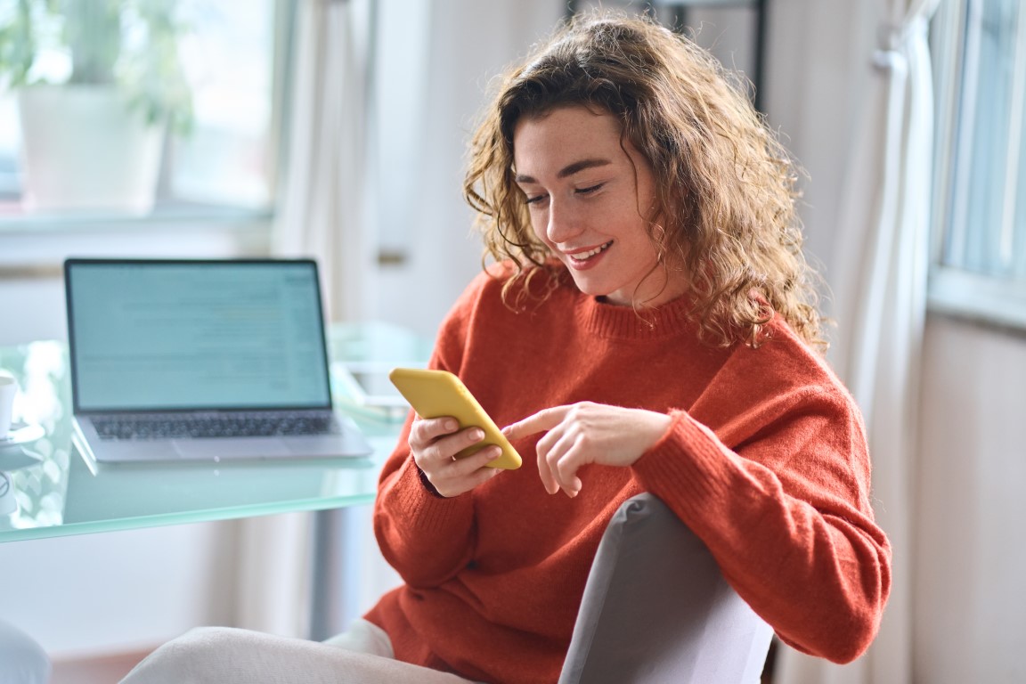 Person looking at their phone at a desk with a laptop on it