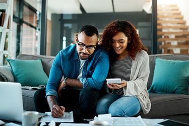 Couple sitting on sofa looking at laptop and papers